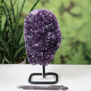 Dark purple Uruguay amethyst druse on metal stand with a pen for scale, showcasing intense sparkle and regular crystal formation.