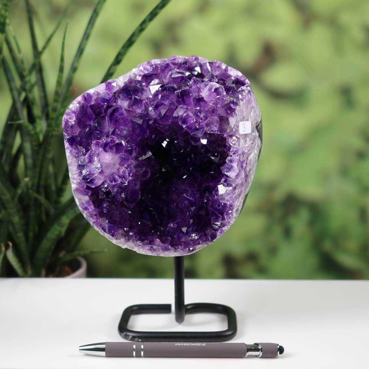 Dark purple Uruguay amethyst druse geode on metal stand with pen for scale, showcasing intense sparkle and regular crystal patterns.