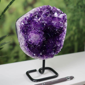 Dark purple Uruguay amethyst geode on black metal stand against a blurred green background