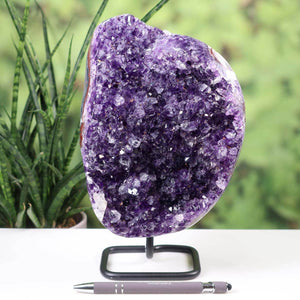 Dark purple Uruguay Amethyst Druse on metal stand displayed on desk with pen and plant in background