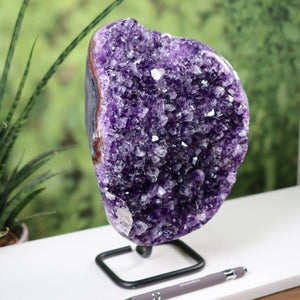 Dark purple Uruguay Amethyst Drusen Geode on metal stand displayed on a white table, showcasing its intense sparkle and regular crystal pattern.