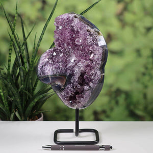 Deep purple Uruguay Amethyst Drusen geode displayed on a metal stand with lush green background and pen for scale