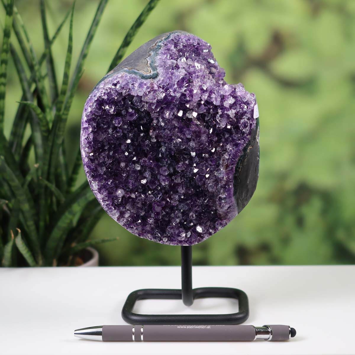 Dark purple Uruguay Amethyst geode on metal stand, exhibited as a unique decorative piece on a table, enhancing indoor decor.