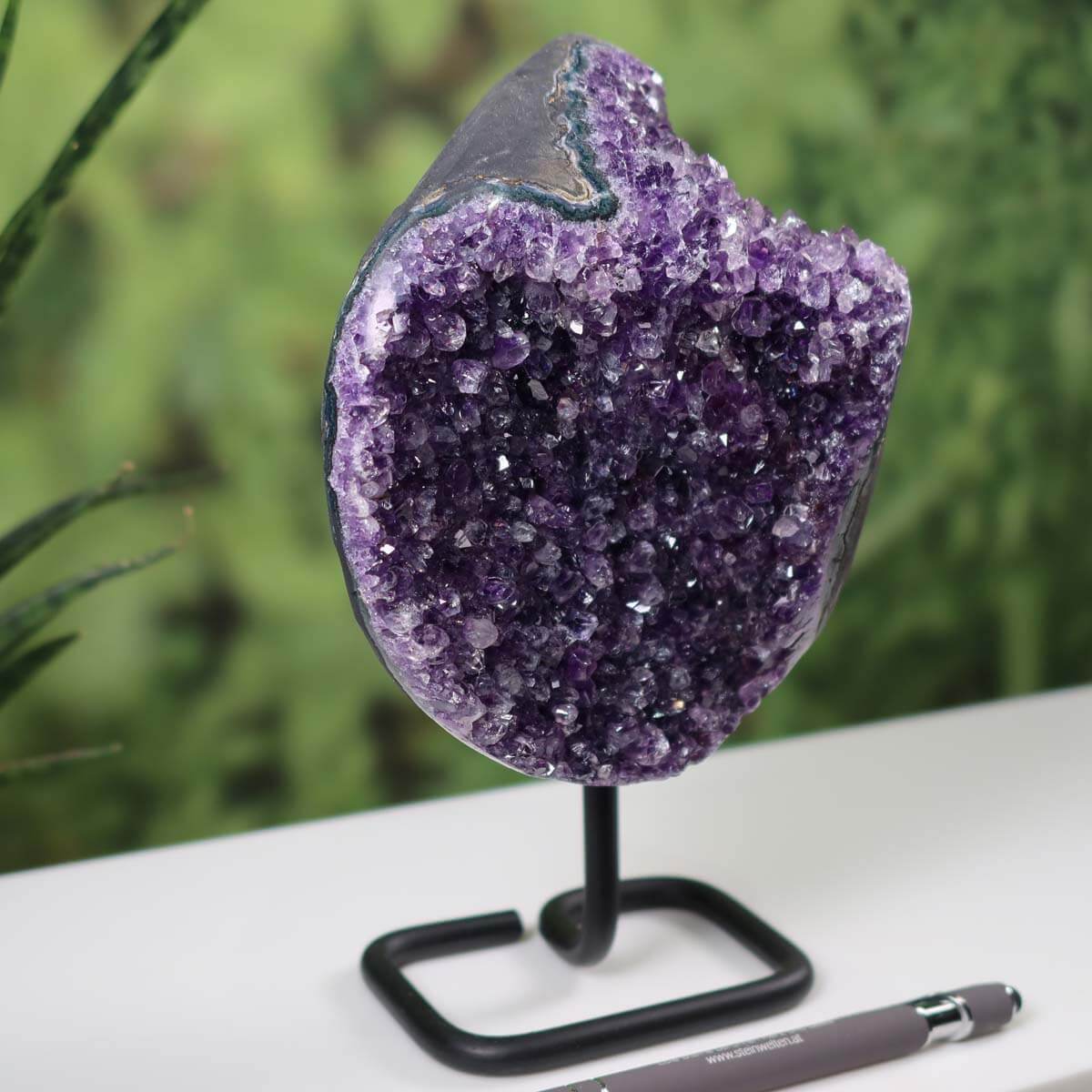 Dark purple Uruguay Amethyst geode on metal stand, exhibited as a unique decorative piece on a table, enhancing indoor decor.