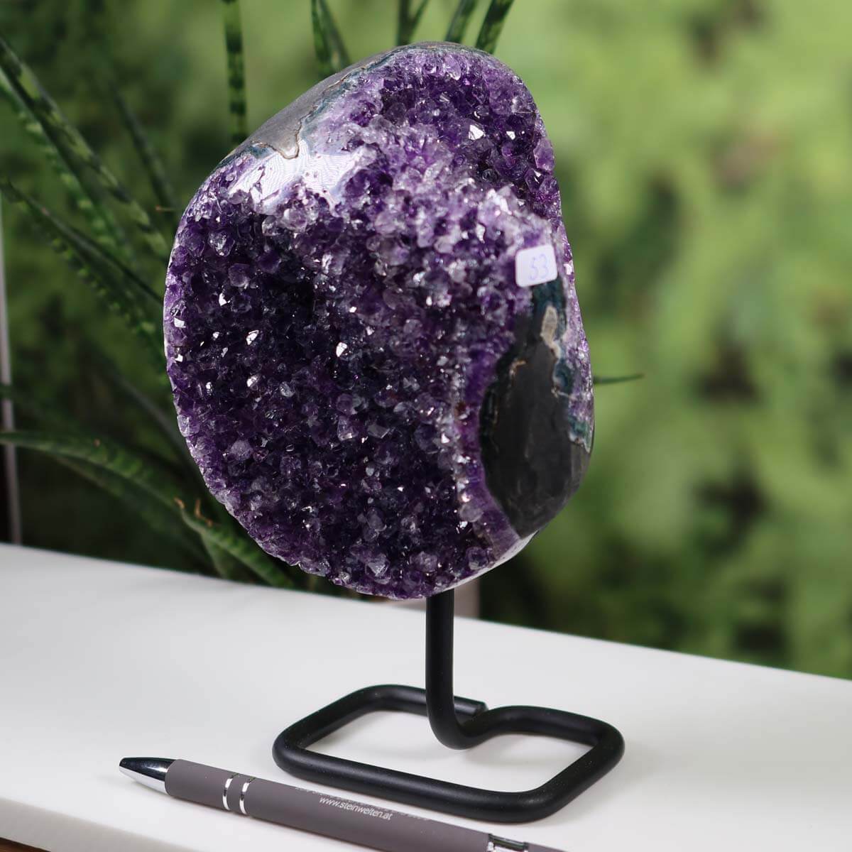 Uruguay Amethyst Druse on metal stand displayed on white table, exemplifying intense dark purple crystals and natural sparkle.