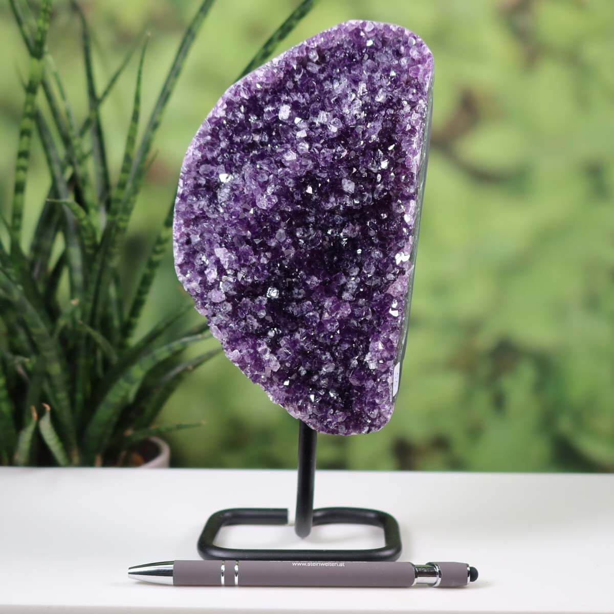 Dark purple Uruguay Amethyst Drusen Geode on metal stand displayed on a table with a pen for scale