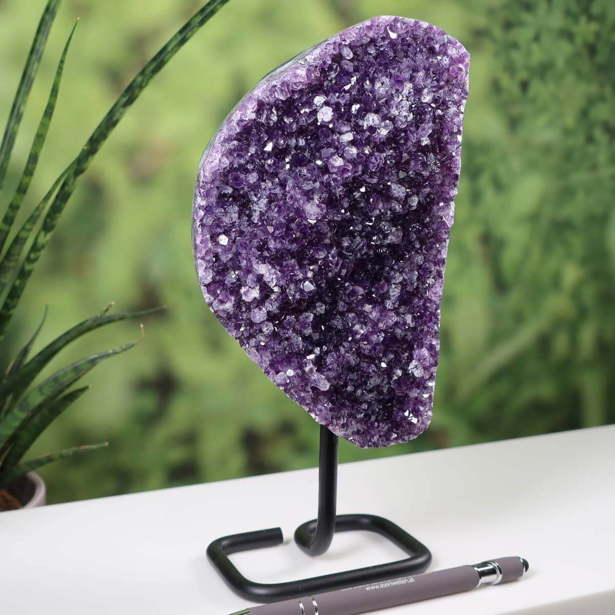 Dark purple Uruguay Amethyst Drusen Geode on metal stand displayed on a table with a pen for scale