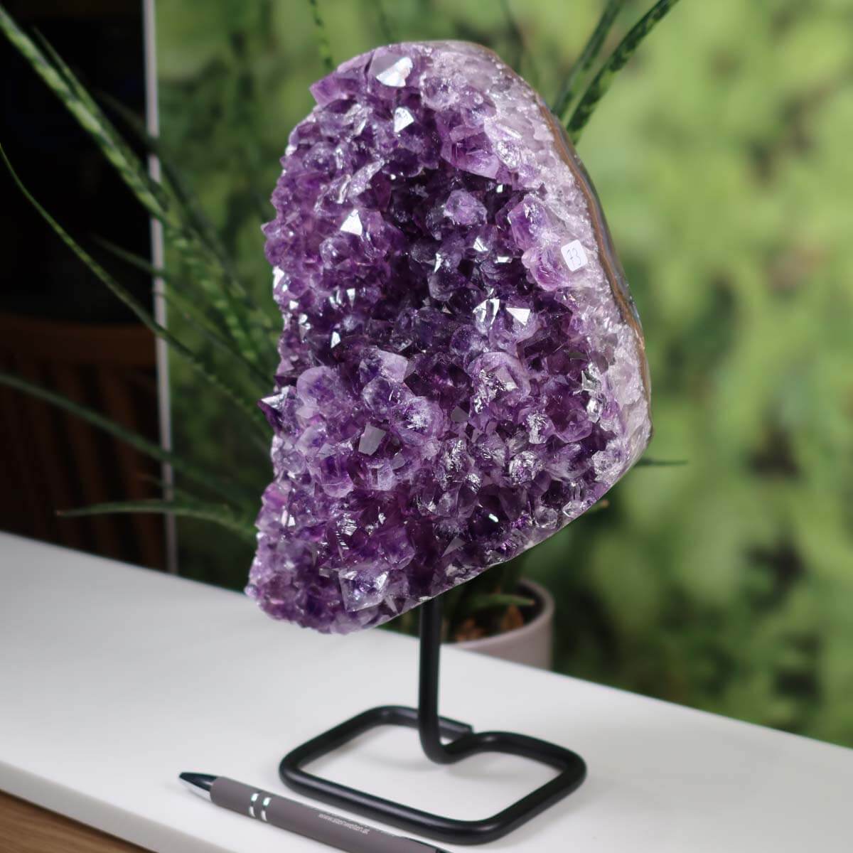 Deep purple Uruguay Amethyst geode displayed on a black metal stand, showcasing intensely sparkling natural crystals.