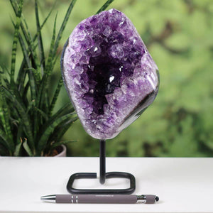 Stunning Uruguay amethyst geode on metal stand with deep purple crystals, displayed on a white surface next to a pen for scale