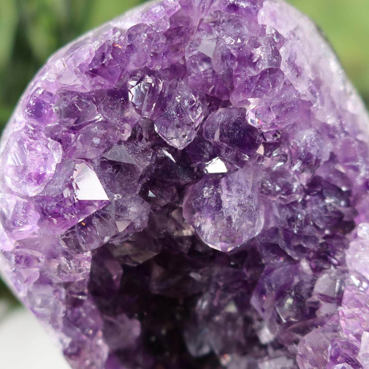 Stunning Uruguay amethyst geode on metal stand with deep purple crystals, displayed on a white surface next to a pen for scale