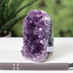 Intense purple Uruguay Amethyst mini geode marked as unique piece number 13 on a white table with green plant background.