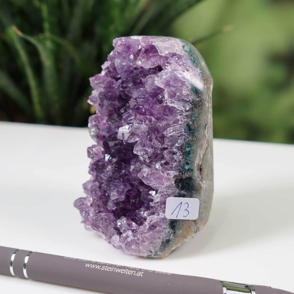 Intense purple Uruguay Amethyst mini geode, labeled "13", displayed on a white surface with a pen for scale.