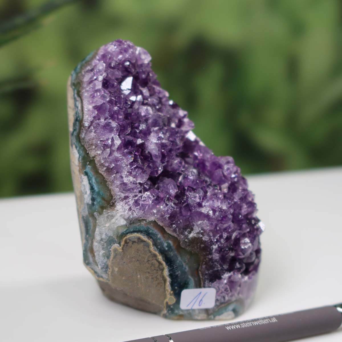 Uruguay Amethyst Mini Geode with intense purple crystals, unique piece number 16 displayed on a white surface with a pen for scale.