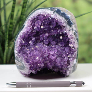 Intensely colored Uruguay Amethyst Mini Geode with dark purple crystals, displayed outdoors with a pen for scale