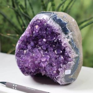 Uruguay Amethyst Mini Geode with vibrant purple crystals, unique item number 18, displayed outdoors next to a pen for scale