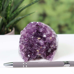 Dark purple Uruguay Amethyst mini Geode NR-2 on a white surface with a pen for scale, vibrant crystals from Steinwelten.