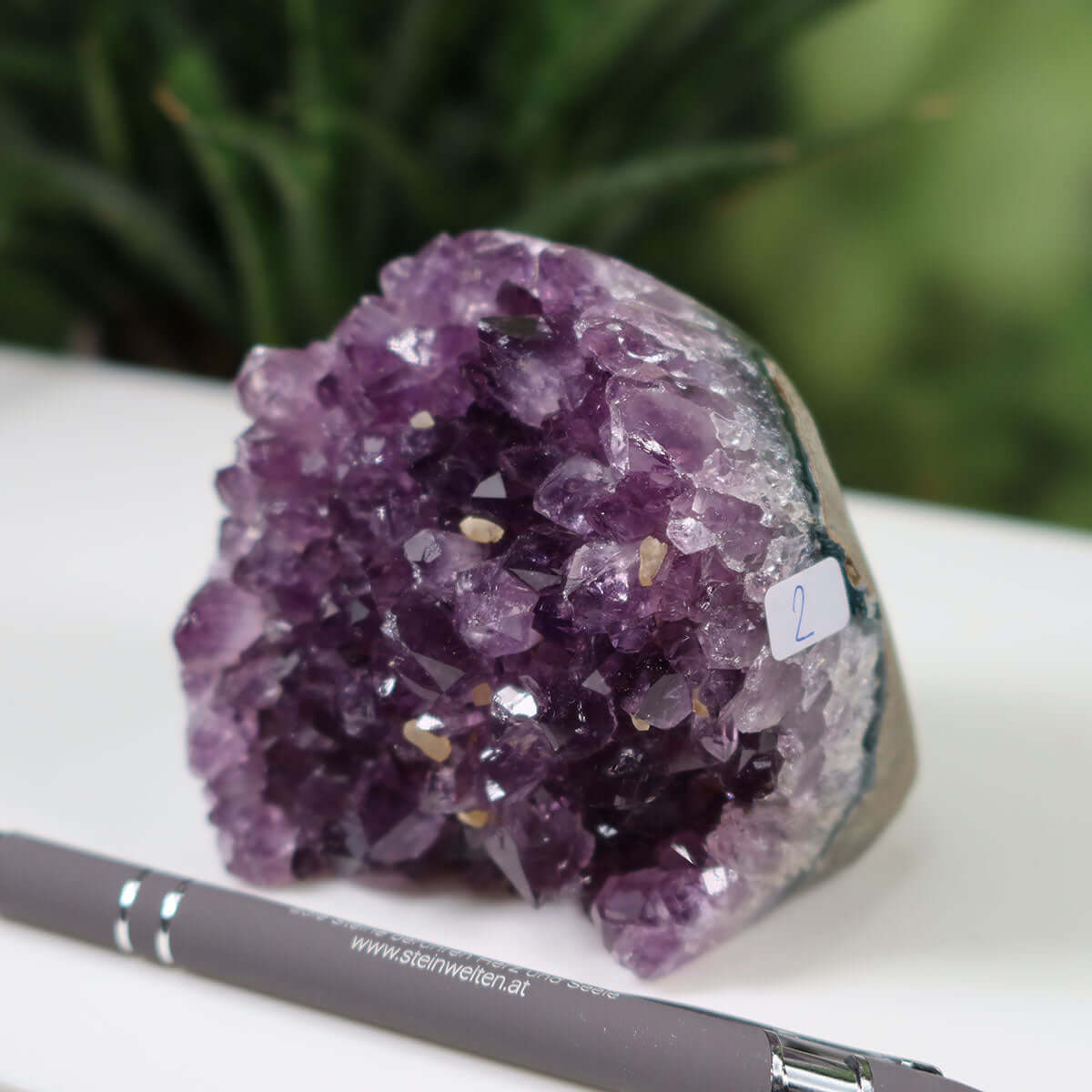 Uruguay Amethyst mini Geode NR-2 with deep purple crystals displayed on a white surface, showcasing its intense sparkle and regular crystal formation.