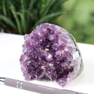 Deep purple Uruguay Amethyst mini Geode NR-2 on a white surface with a pen for scale, showcasing intense crystal clusters.