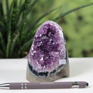 Uruguay Amethyst Mini Geode Number 32 with intense violet crystals displayed beside a pen on a desk with green plant background.