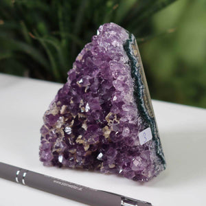 Uruguay Amethyst Mini Geode with intense purple crystals and deep green outer layer, labeled "Unikat NR 3" on white surface with pen for scale.