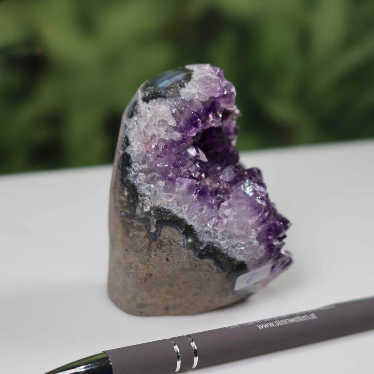 Uruguay Amethyst mini geode with intense purple crystals displayed next to a pen for scale on a white surface.