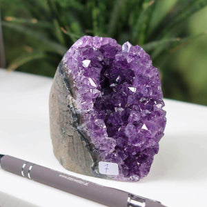 Uruguay Amethyst Mini Geode with vibrant deep purple crystals, unique piece number 7, displayed on white surface with a pen for scale