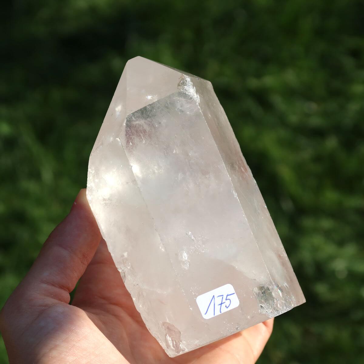 Hand holding polished Bergkristall Quarz Crystal Point Nr.175 from Brazil for meditation, 10x6 cm, reflecting light with clarity.