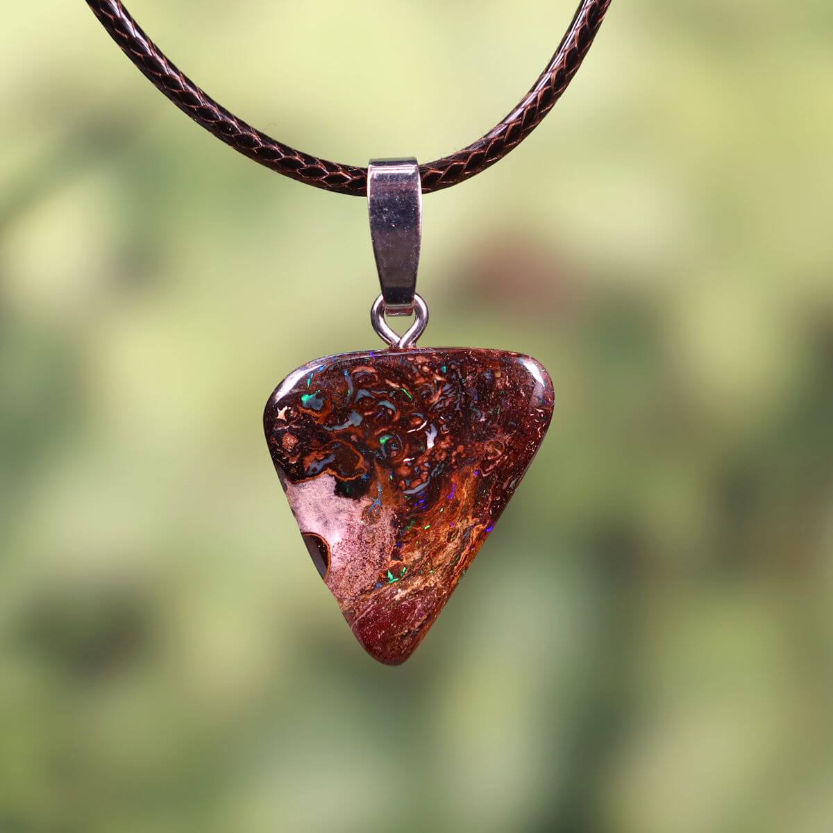 Unique hand-polished Boulder Opal pendant number 308 with a solid silver loop, hanging on a brown leather cord against a natural green background