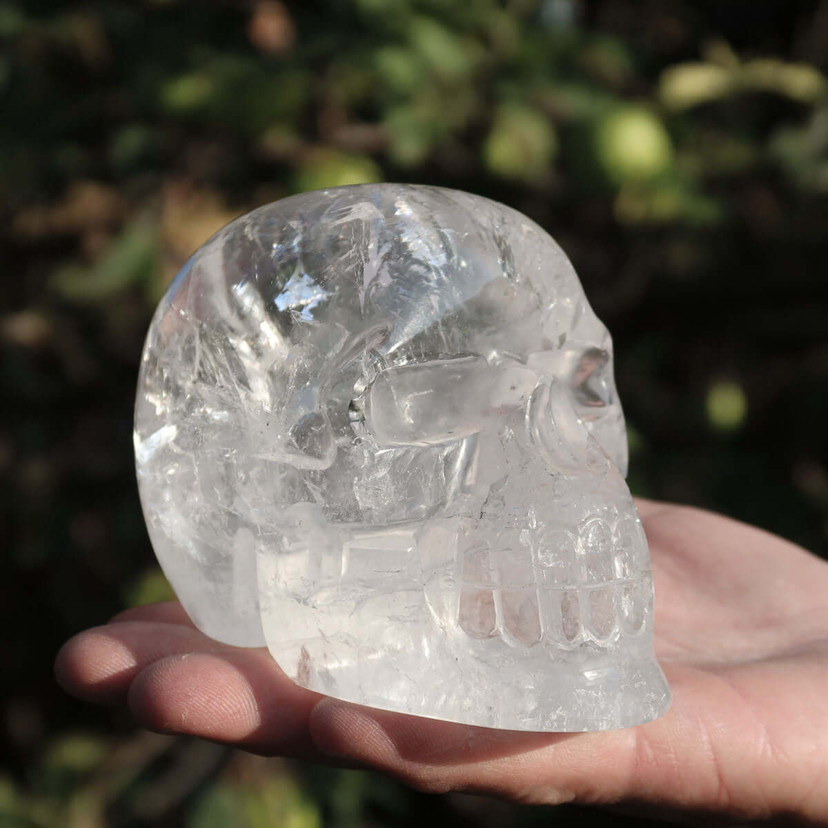 Handmade quartz crystal skull held in a hand, showcasing its clarity and intricate details in natural light.