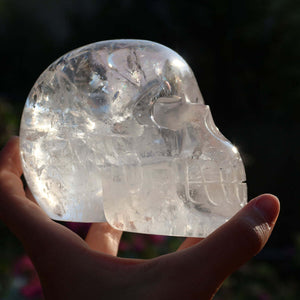 Hand holding a unique handcrafted clear quartz crystal skull in sunlight, showcasing intricate details and clarity.