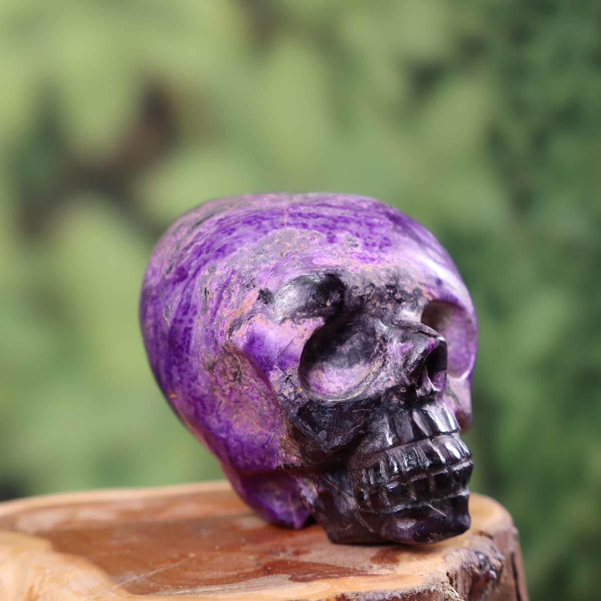 Handcrafted Sugilith crystal skull collectible, made from a single gemstone, displayed on wooden surface, with vibrant purple hues
