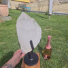 Natürlicher Bergkristall XL am Drähständer und Flasche Sekt im Freien, ideal für Yoga-Studios und Innenarchitektur.