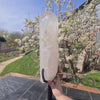 Natürlicher Bergkristall XL auf Metallständer im Freien, umgeben von blühenden Bäumen, ideal für Raumdekoration und Meditation.